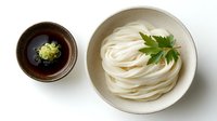 Fresh udon noodles served in ceramic bowl with wasabi and green garnish on white background, traditional Japanese cuisine presentation for menu or cookbook.