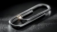 Shiny metallic paper clip on dark textured surface with dramatic lighting for office supplies and business organization concepts.