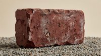 Red clay brick with weathered texture and porous surface on gravel ground, construction material for building and masonry projects isolated on neutral background.