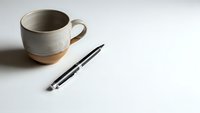 Minimalist workspace with handcrafted ceramic coffee mug and black pen on clean white surface for creative writing and morning productivity routines.