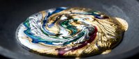 Abstract golden swirl with colorful paint mixing in circular motion on dark surface creating artistic fluid dynamics for creative projects.