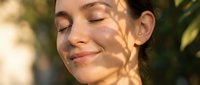 Young woman with closed eyes and serene expression, enjoying natural sunlight and shadow patterns on her face outdoors. Skincare and wellness concept.
