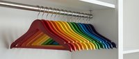 Colorful rainbow wooden coat hangers arranged in gradient spectrum on closet rod, organized wardrobe storage solution for home organization and decluttering.