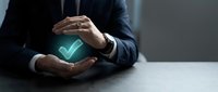 Professional businessman in dark suit protecting glowing green checkmark symbol with hands, representing quality assurance, approval and business success.