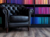Luxurious black leather armchair with tufted back and silver studs against colorful bookshelf background on wooden floor, creating elegant reading corner atmosphere.