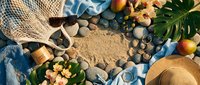 Summer beach vacation flat lay with straw hat, tropical leaves, seashells and smooth stones on sandy background for travel and holiday concepts.