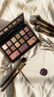 Luxury makeup palette with eyeshadows and blush alongside professional brushes on elegant fabric background for beauty and cosmetics styling.