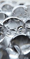 Macro view of water drops on metallic silver surface creating abstract reflective patterns and curved shapes. Artistic close-up showing liquid transparency and light play.