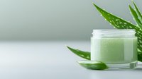 Fresh aloe vera cosmetic cream in glass jar with natural plant leaves on light background, organic skincare and beauty product concept.