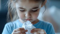 Young girl in light blue sweater holding and examining whipped cream with curiosity, close-up portrait with soft dreamy atmosphere and natural lighting.