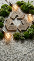Wooden recycle symbol surrounded by green moss and glowing Edison bulbs on stone surface, representing sustainable energy and eco-friendly concepts.