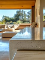 Modern kitchen island with white speckled countertop and wooden accents overlooking garden view through large window in contemporary home interior design.