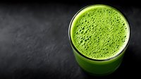 Fresh green smoothie with foam in glass on dark slate background for healthy lifestyle and nutrition concepts.