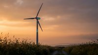 Wind turbine generating clean renewable energy at golden sunset with wildflowers and grass in foreground creating sustainable power for environmental conservation.