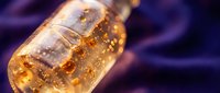 Golden amber liquid with bubbles in glass bottle against blurred purple background, suitable for beverage, alcohol, or product photography and advertising campaigns.