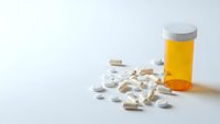 White prescription pills scattered beside orange medication bottle on clean surface for healthcare and pharmaceutical concepts.