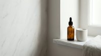 Amber glass dropper bottle and white ceramic jar on marble windowsill with natural light, skincare and wellness product display for cosmetics, beauty, and home decor design projects.