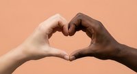 Two diverse hands forming heart shape symbol representing unity love and friendship against warm peach background for social campaigns and diversity projects.