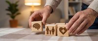 Professional man arranging wooden blocks with health symbols including brain, family and heart icons on desk for wellness concept planning.