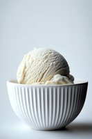 Creamy vanilla ice cream scoop served in elegant white ribbed ceramic bowl against light background, minimalist food photography composition for dessert menus.