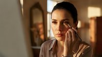 Young Hispanic woman applying makeup with brush in warm morning light at home getting ready for work day.