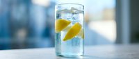 Refreshing glass of sparkling water with lemon slices and ice cubes on a light surface, soft blue background, healthy drink concept.