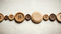 Wooden buttons in various sizes arranged in a row on neutral fabric background, featuring natural wood tones and four-hole designs for sewing and crafting projects.