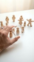 Hand holding transparent glass cube with wooden figure inside while other wooden people stand nearby representing team selection and leadership concepts.