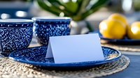 White blank card on blue patterned ceramic plate with matching teacup, fresh lemons and green plant creating elegant table setting for mockup designs.