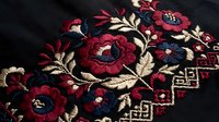 Traditional folk embroidery with red roses and floral motifs on dark fabric, showcasing intricate needlework and cultural textile art for craft projects.