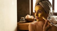 Young woman applying facial serum with dropper in spa bathroom wearing towel turban after shower for skincare routine and wellness self-care ritual.