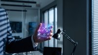 Businessman in dark suit holding glowing purple holographic cube with digital interface in modern office workspace, representing technology innovation and business solutions.