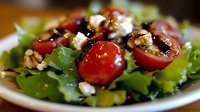 Fresh green salad with cherry tomatoes, crumbled feta cheese, walnuts and balsamic glaze on white plate, close up view of healthy Mediterranean dish.