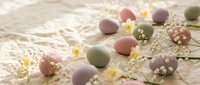 Pastel colored Easter eggs with spring flowers and decorative pearls arranged on soft lace fabric creating festive holiday composition for seasonal celebrations.