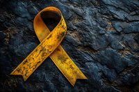 Golden awareness ribbon symbol on dark textured stone surface representing support, hope and solidarity for various causes and charitable campaigns.