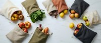 Reusable cotton produce bags filled with fresh vegetables and fruits arranged on marble surface, promoting sustainable zero waste grocery shopping.