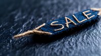 Torn blue denim fabric label with gold embroidered SALE text on dark textured background, dramatic lighting and shallow depth of field for retail promotion.