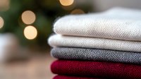 Folded linen fabric layers in white, gray and burgundy colors with soft bokeh lights in background creating cozy autumn or winter mood for home decor and textile design.