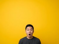 Surprised young man with dark hair and olive complexion wearing black shirt against bright yellow background, expressing shock or amazement.