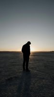 Silhouette of contemplative man standing alone on vast salt flat during golden hour sunset with dramatic sky and distant mountains creating peaceful solitude scene.