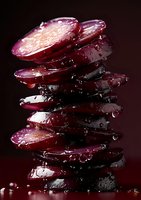 Fresh sliced beets stacked in tower formation with water droplets on dark background, dramatic lighting highlights deep purple-red color and moist texture.