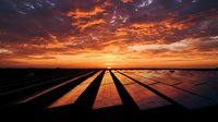 Solar panel farm at sunset with dramatic orange and golden sky, casting long shadows across renewable energy installation for sustainable power generation and clean technology concepts.