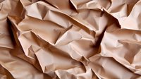 Crumpled beige paper background with rough textured surface showing natural folds and creases, creating abstract geometric patterns and shadows.
