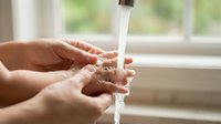 Clean fresh water flowing from faucet into cupped hands for drinking and hygiene in bright kitchen setting with natural window light.