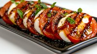 Fresh caprese salad with ripe tomatoes, mozzarella cheese and basil leaves drizzled with balsamic glaze on dark plate for Italian cuisine and healthy eating.