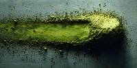 Green matcha tea powder scattered on dark surface creating organic texture for culinary and wellness designs.