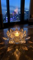 Crystal lotus flower candle holder glowing on marble surface with blurred city lights through window creating peaceful meditation atmosphere for home decor.