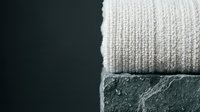 Folded cream knit sweater draped over dark stone surface, minimalist composition with negative space for design layouts, fashion and lifestyle content.