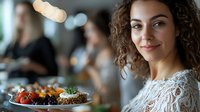 Young mixed-race woman with curly hair smiling while holding healthy breakfast bowl with berries and granola in modern cafe restaurant setting.