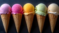Colorful ice cream scoops in waffle cones arranged in row showing variety of flavors including strawberry, raspberry, mango, pistachio and vanilla on dark background.